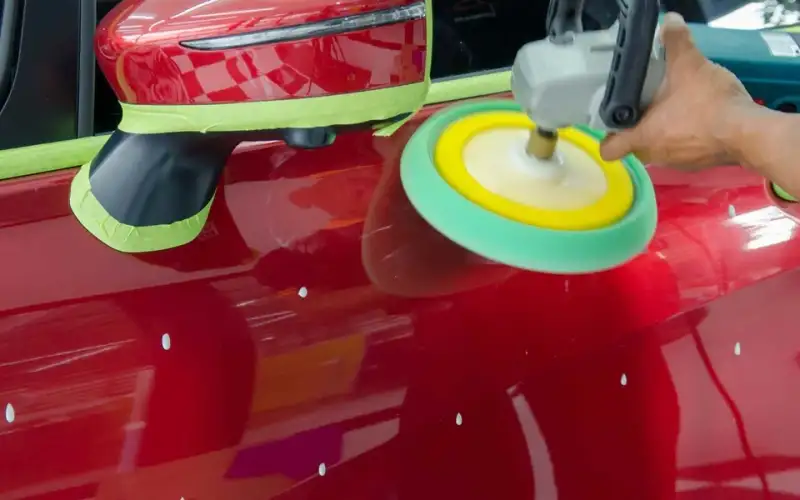 Polisher with a yellow pad working a red car panel
