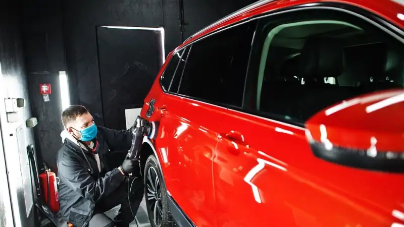 Technician polishing a red car in a paint booth