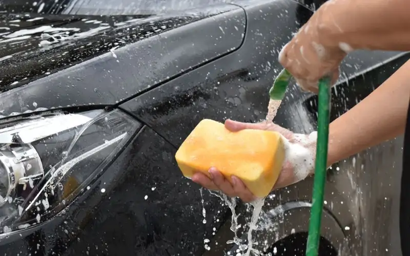 Hand washing a black car with a yellow sponge