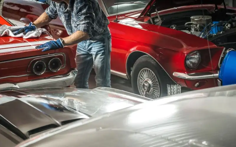 Man waxing a red classic Mustang with the hood open