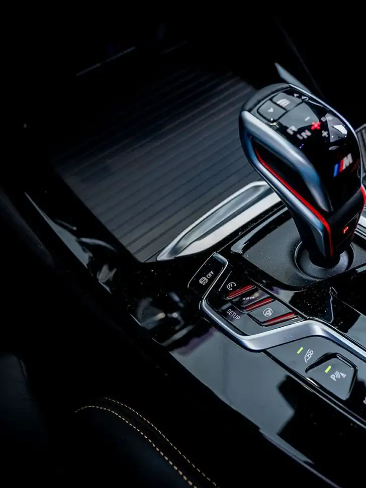 Gear shift and center console of a dark car interior, lit by a single soft highlight