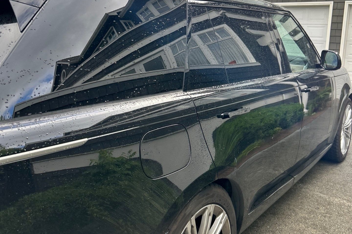 Sharp reflection of a house and hedge held in the corrected black paint of a Range Rover