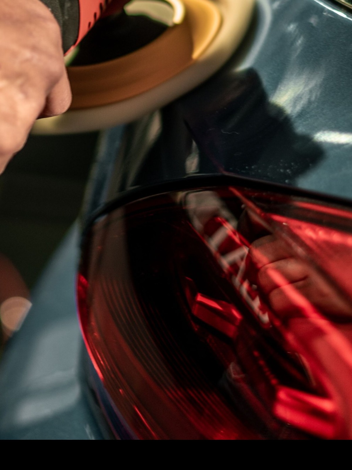 Foam polishing pad working across a dark rear panel beside the taillight