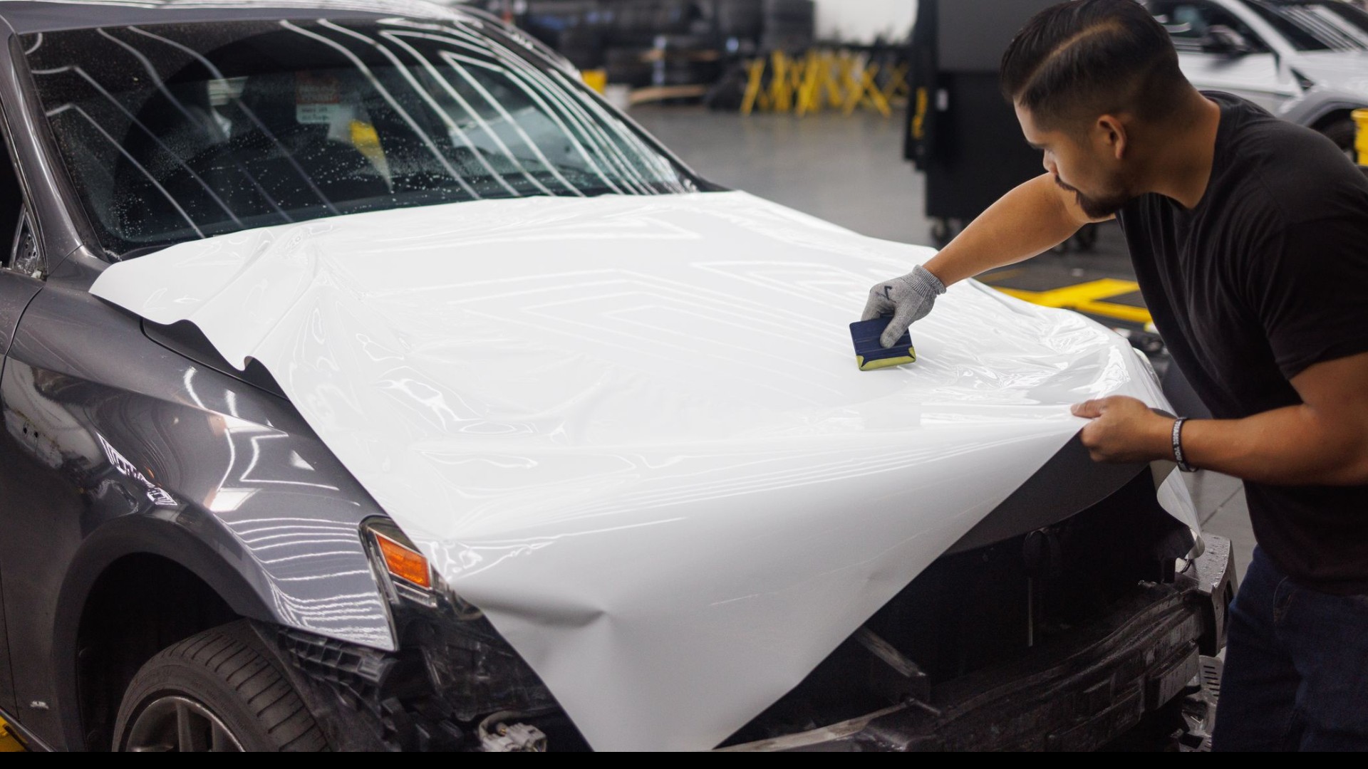 Technician squeegeeing paint protection film across a vehicle hood