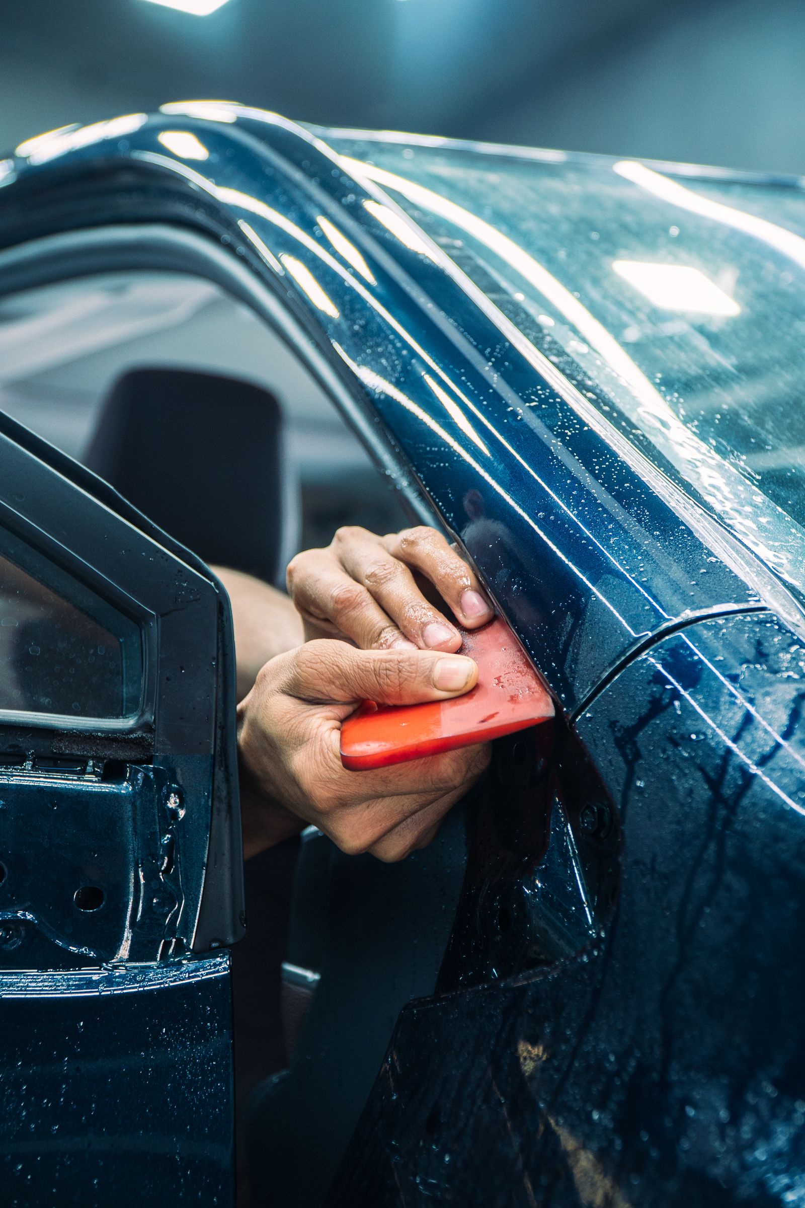 Hands using a squeegee to smooth window film along a car door glass edge