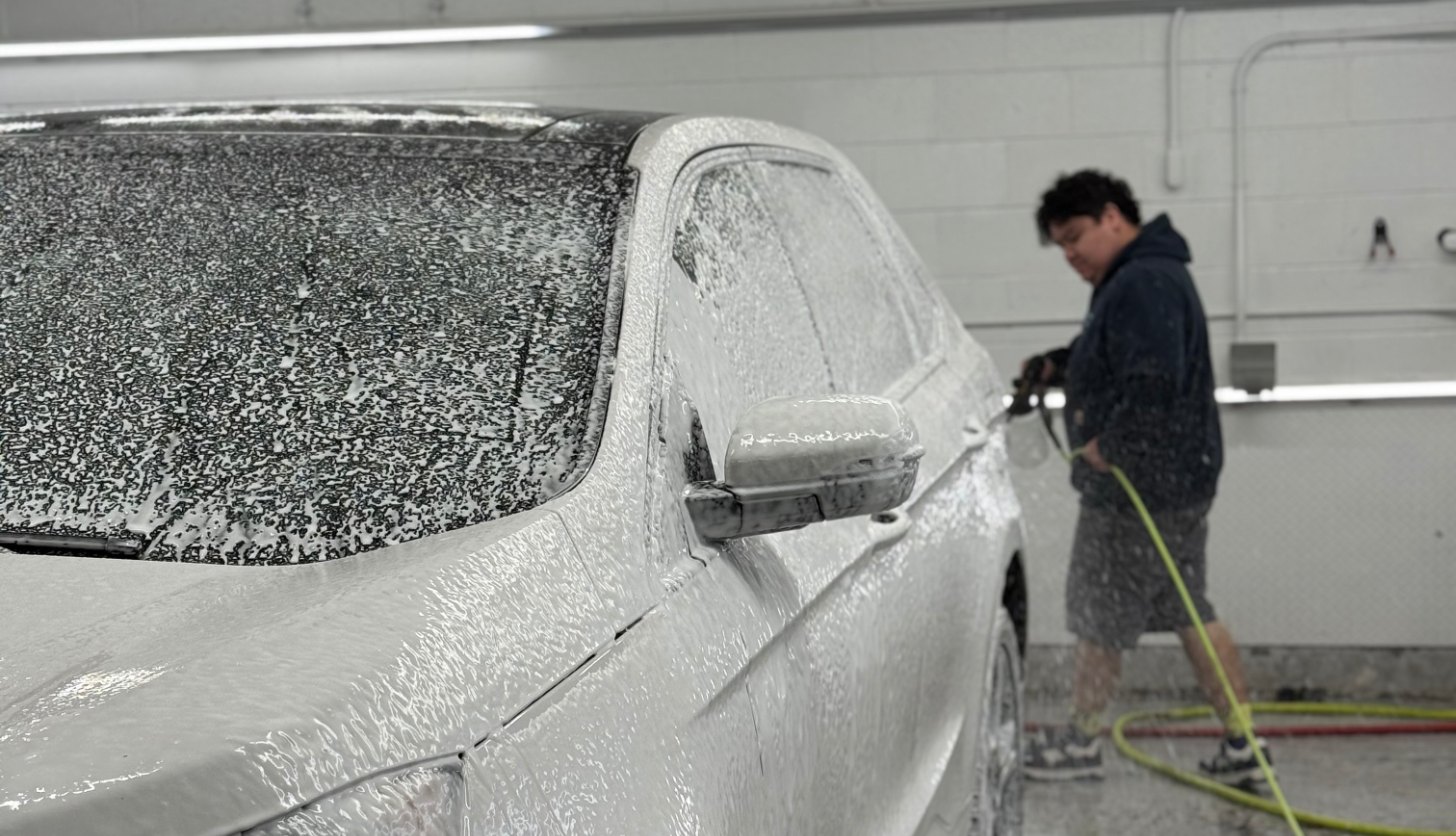 Eco Car Cafe detailer hand washing a foam-covered vehicle in the detailing bay
